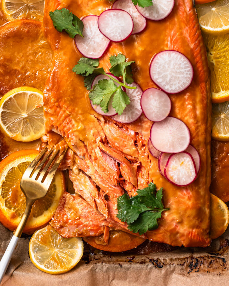 Citrus miso butter salmon side on a baking sheet with slices of lemon and orange.