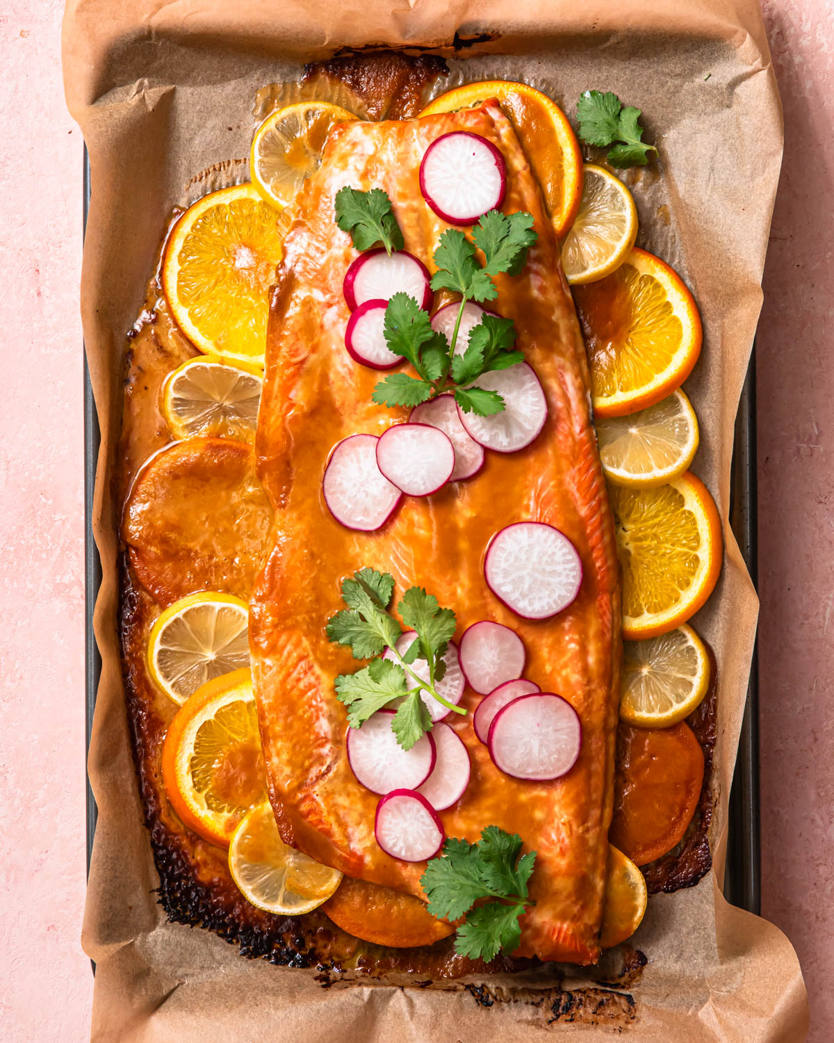 Citrus miso butter salmon side on a baking sheet with slices of lemon and orange.