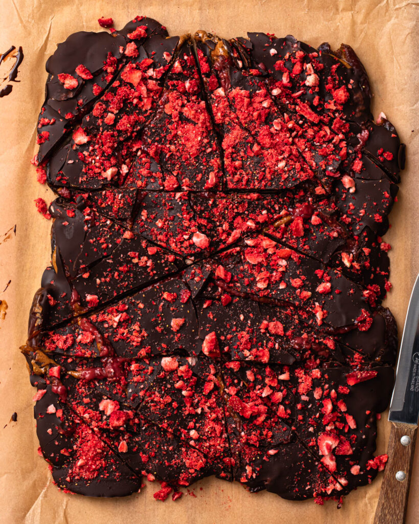 Dark chocolate date bark topped with freeze dried strawberries and chopped into pieces.