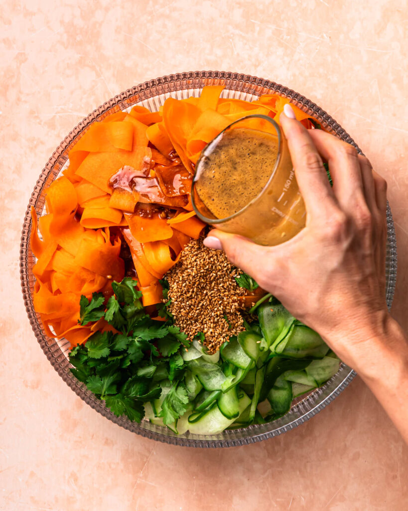 Salad dressing being poured onto vegetables in a salad bowl.
