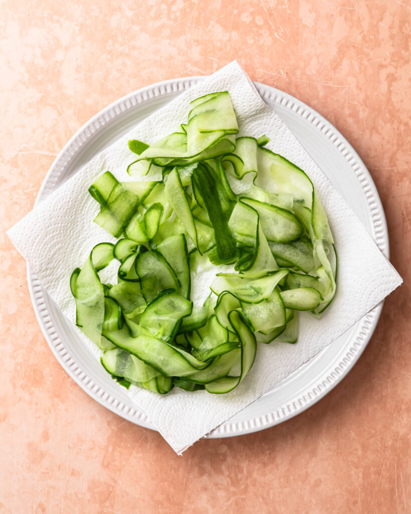 Cucumber ribbons resting on paper towel on a plate.