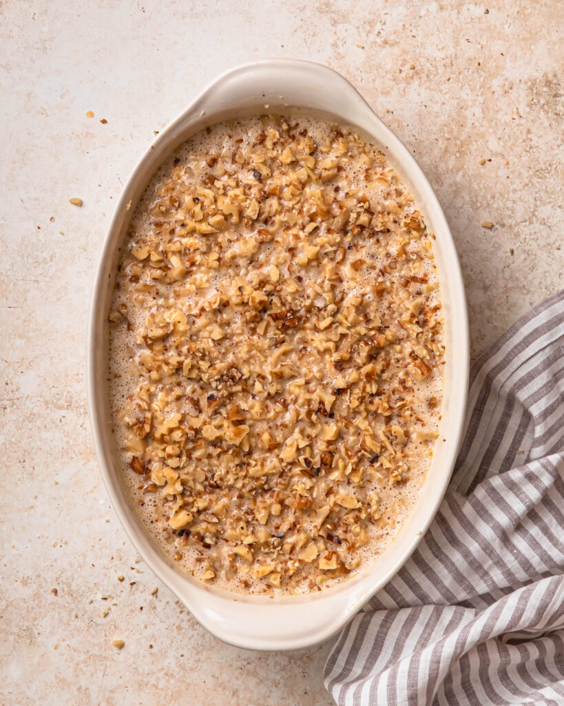 Banana bread baked oats mixture poured into an oval baking dish and topped with chopped walnuts.