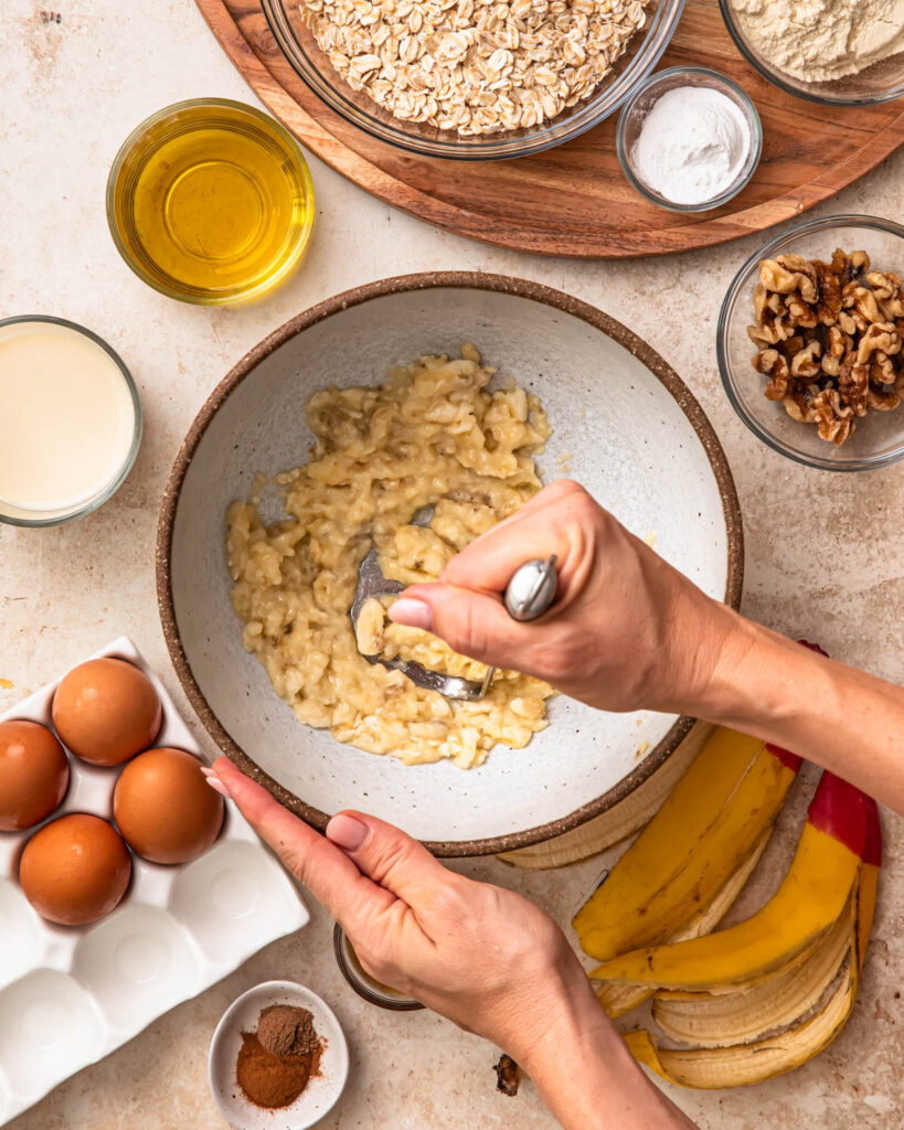 Bananas in a mixing bowl being mashed.