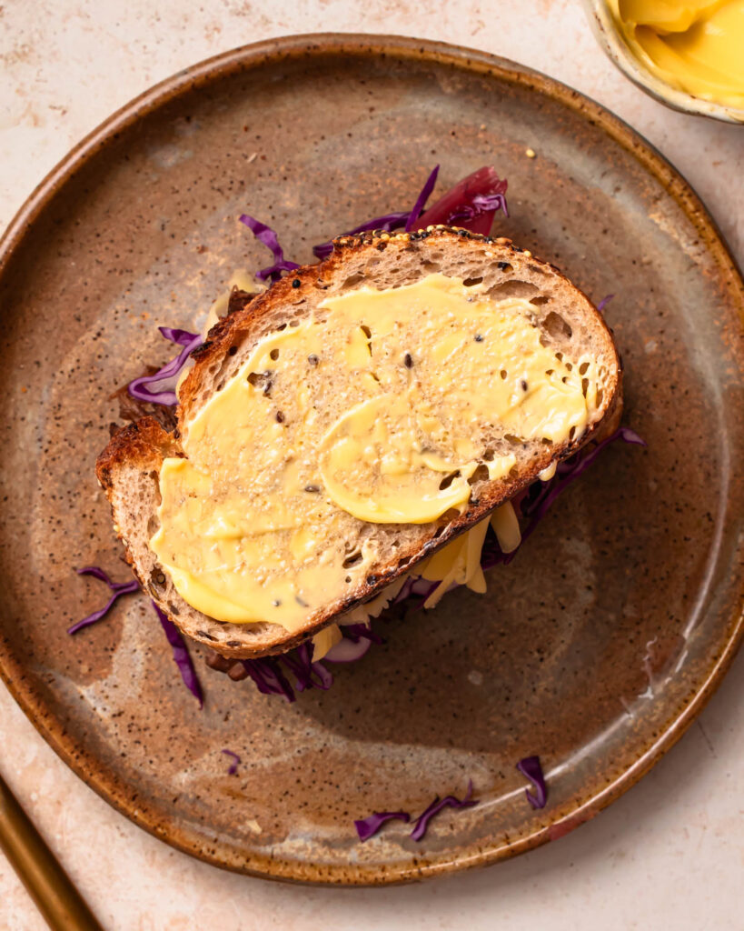 A buttered piece of bread placed on top of a brisket sandwich.