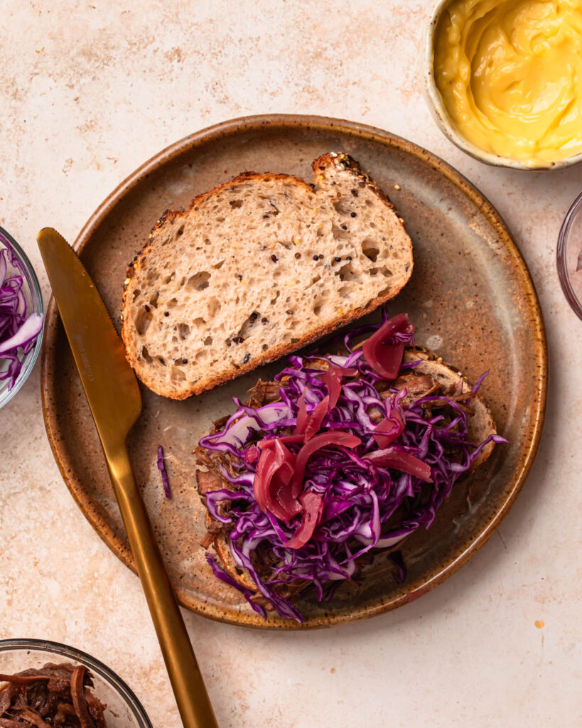 Two slices of bread on a plate, one topped with pulled brisket and shredded red cabbage.