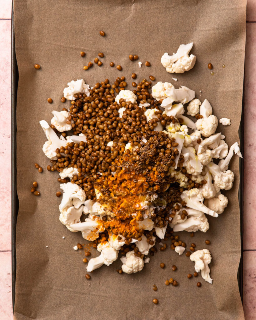 Cauliflower, lentils and spices piled on a baking tray. 
