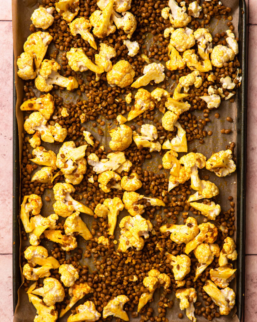 Cauliflower and lentils seasoned with turmeric and other spices and spread out into an even layer on a baking tray.