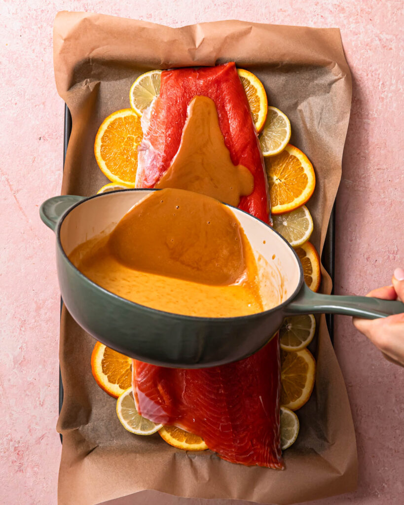 Citrus miso butter sauce in a saucepan being poured onto a large fillet of salmon.