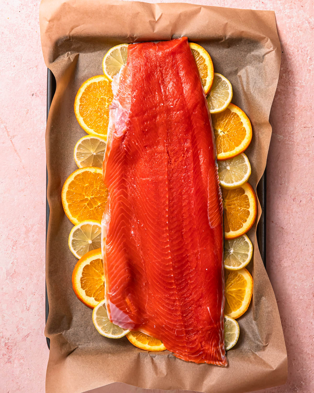 A whole side of salmon resting on top of thin slices of orange and lemon.