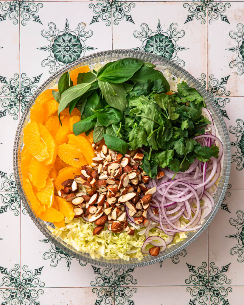 Chopped almonds added to other citrus slaw ingredients in a bowl. 