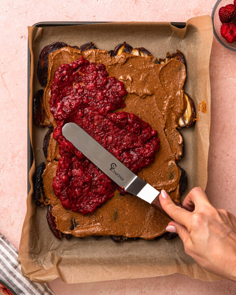 Strawberry chia jam being spread over a layer of almond butter and medjool dates. 