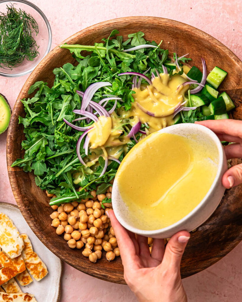 Halloumi avocado salad ingredients in a salad bowl, with dressing being poured over the top.