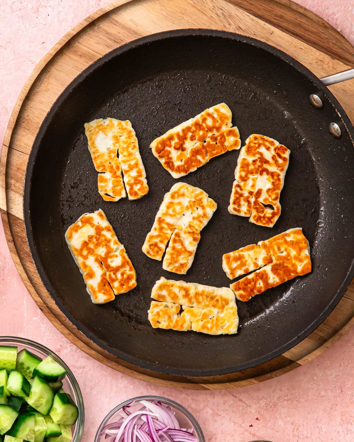 Slices of golden brown halloumi cooking in a frying pan.