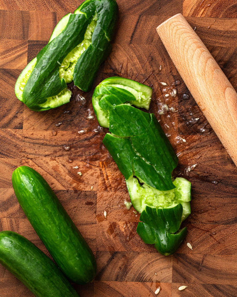 Lebanese cucumbers on a chopping board that have been smashed with a rolling pin. 