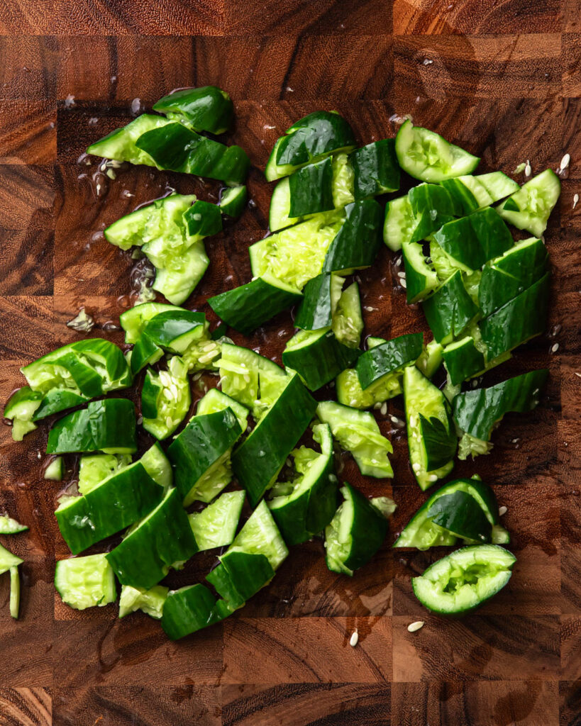 Roughly chopped smashed cucumbers on a chopping board.
