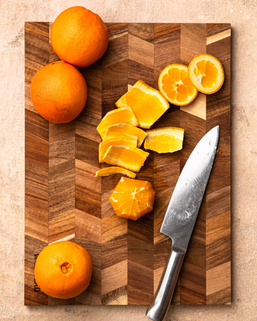 An orange on a chopping board with the peel removed. 