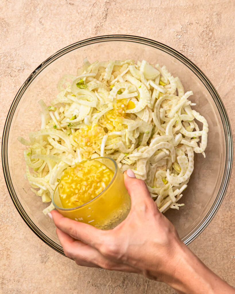 Dressing being poured over sliced fennel in a bowl. 