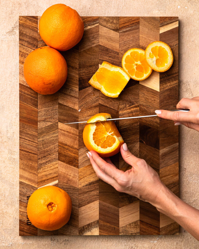 An orange with the top and bottom sliced off and a knife slicing down the side to remove the peel.