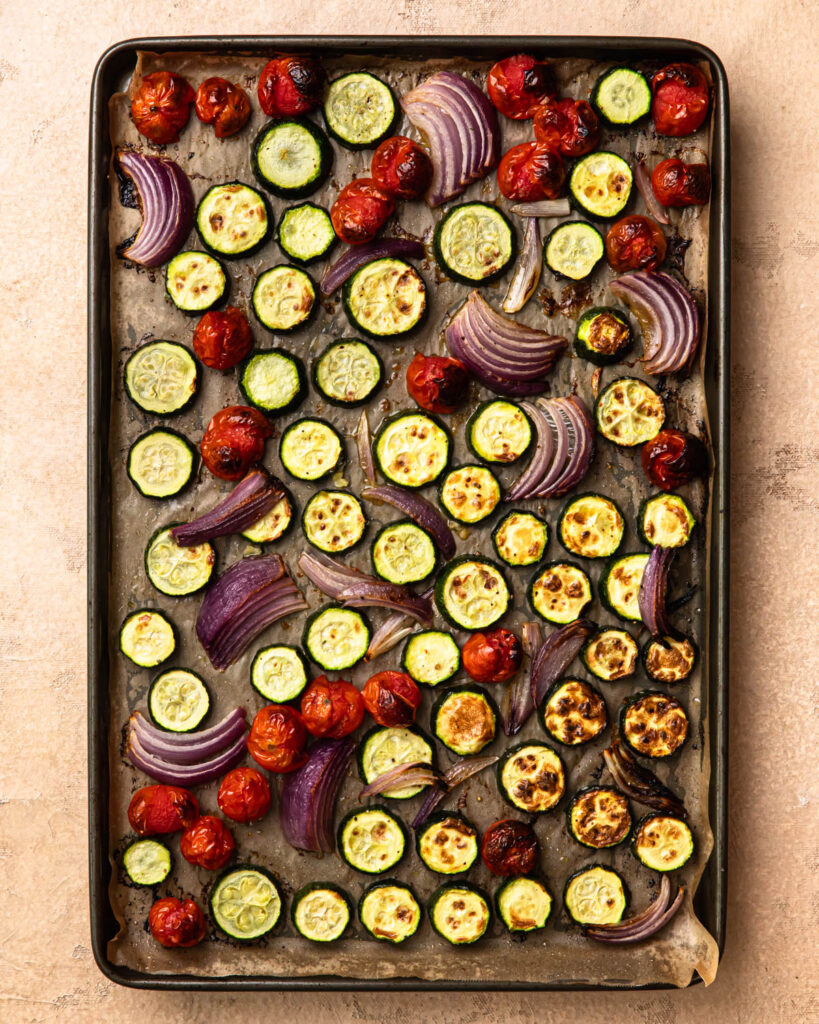 Roasted zucchini, cherry tomatoes and onion wedges on a baking paper lined baking tray.