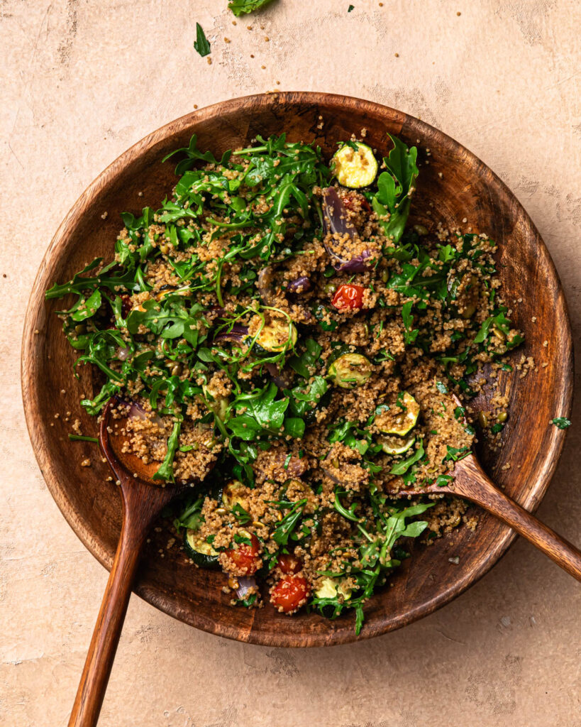 Roasted zucchini and quinoa salad in a large wooden bowl, tossed together. 