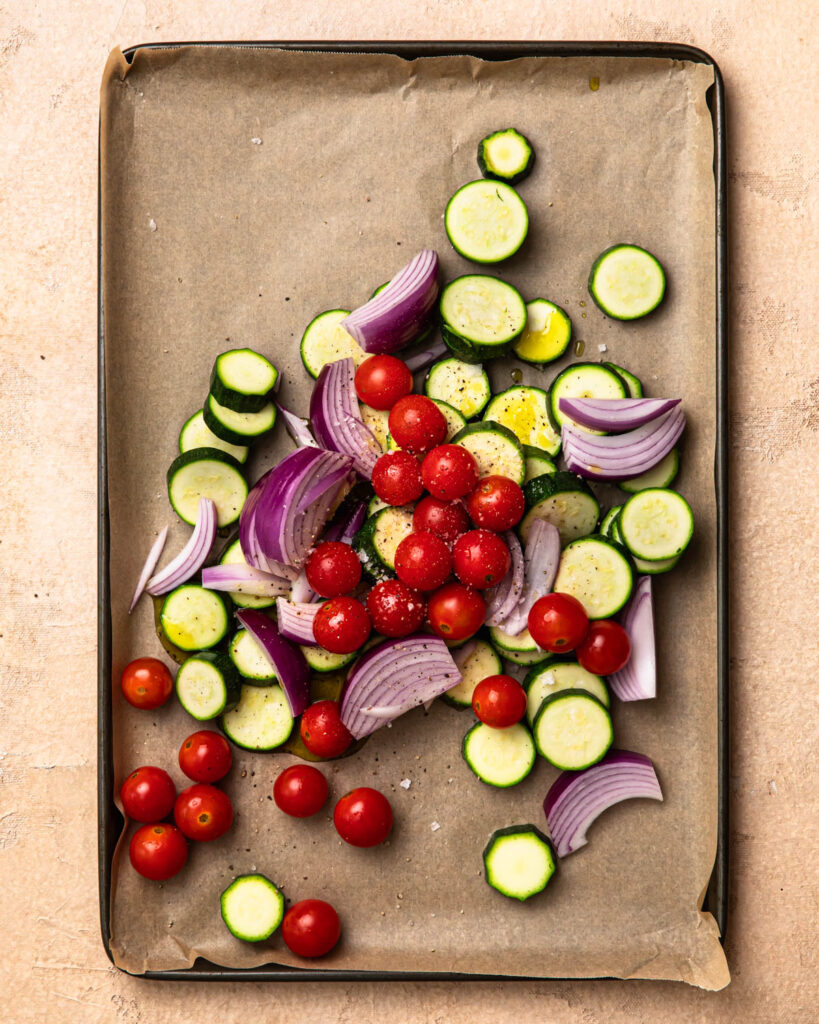 Zucchini rounds, cherry tomatoes and onion wedges on a baking paper lined baking tray.