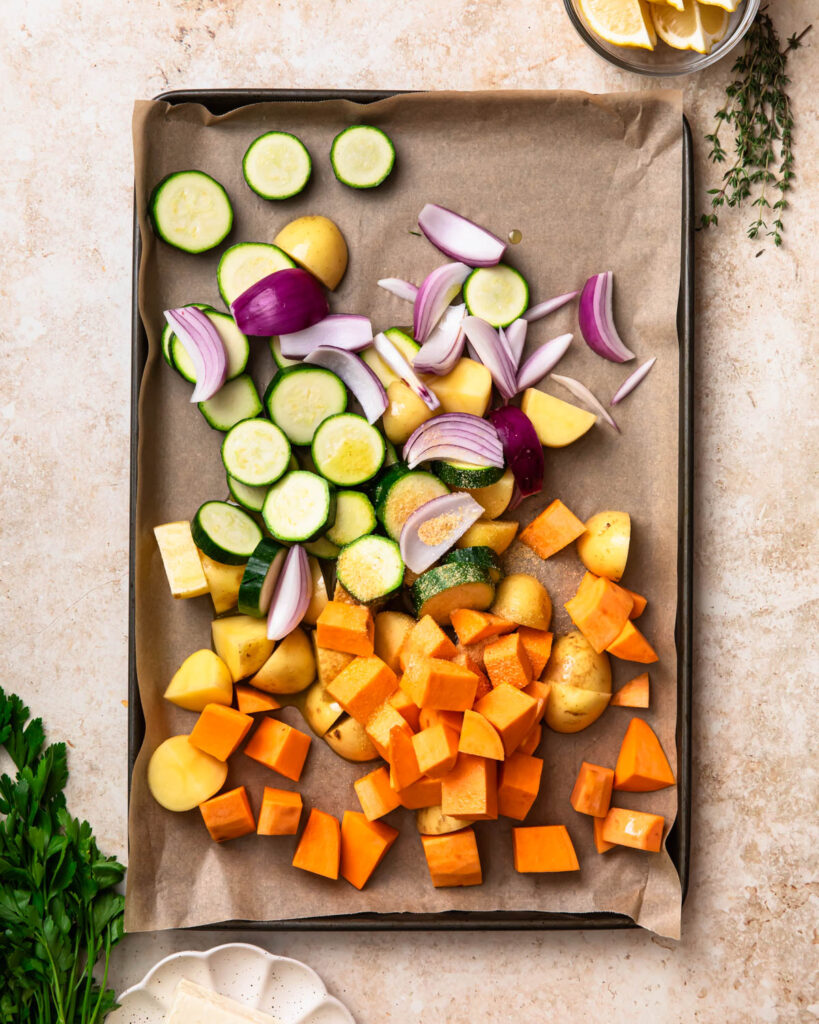 Cut up potatoes, sweet potato, zucchini and red onion added to a large sheet pan and seasoned. 