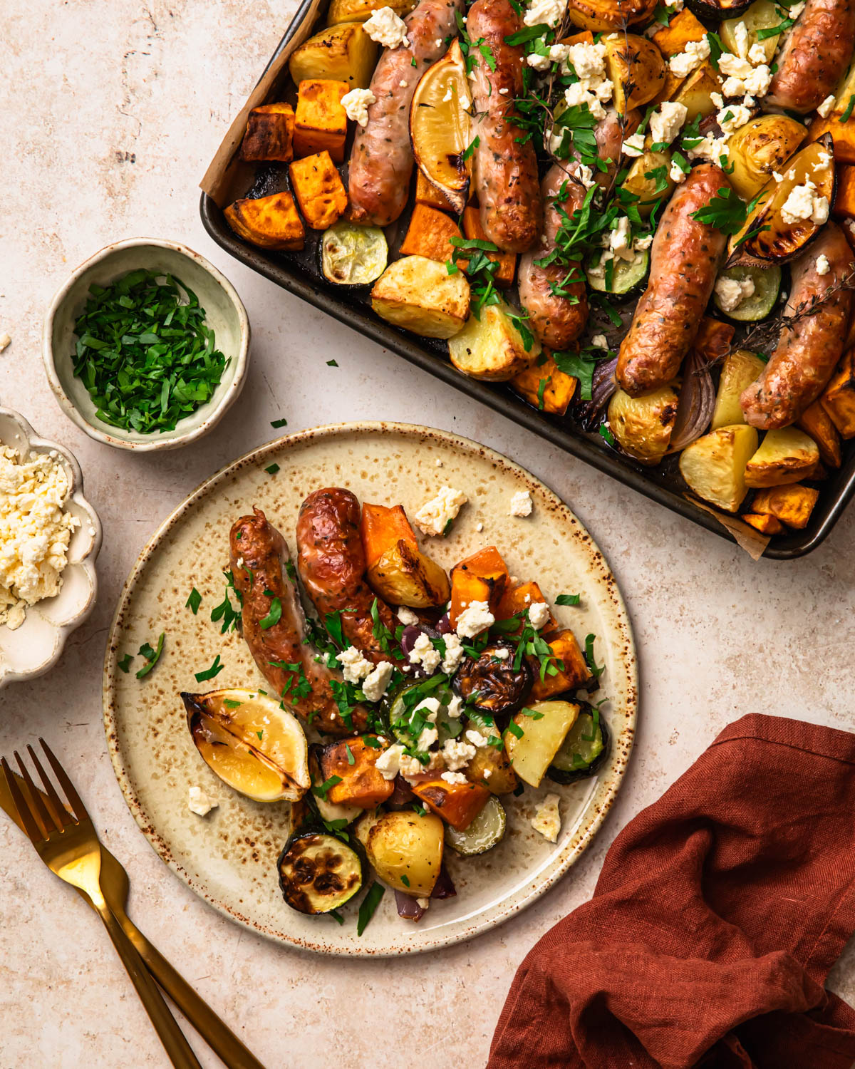 Sheet pan chicken sausages and vegetables served on a plate topped with crumbled feta and chopped parsley.