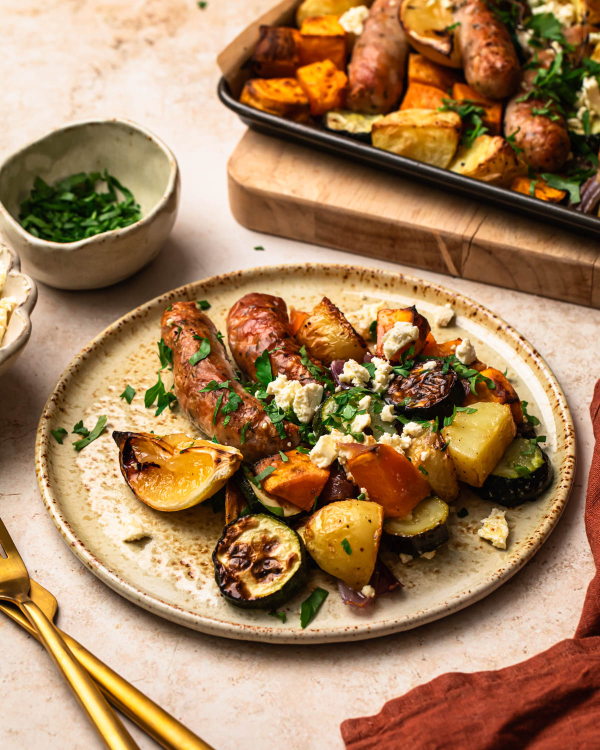 Sheet pan chicken sausages and vegetables served on a plate topped with crumbled feta and chopped parsley.