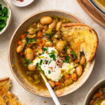 Brothy beans served in a bowl topped with sour cream, herbs and chilli flakes.