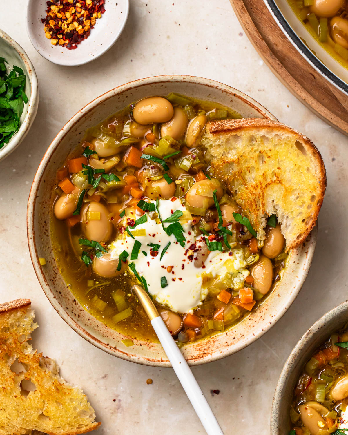 Brothy beans served in a bowl topped with sour cream, herbs and chilli flakes.