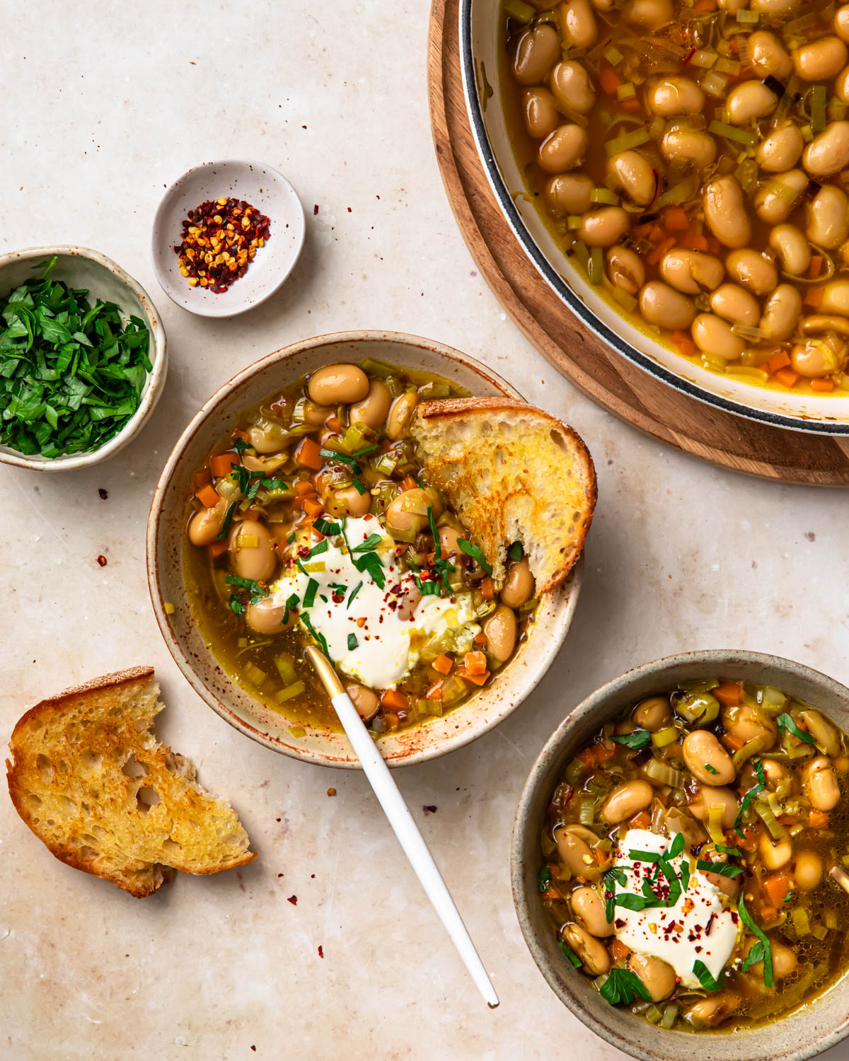 Brothy beans served in a bowl topped with sour cream, herbs and chilli flakes.