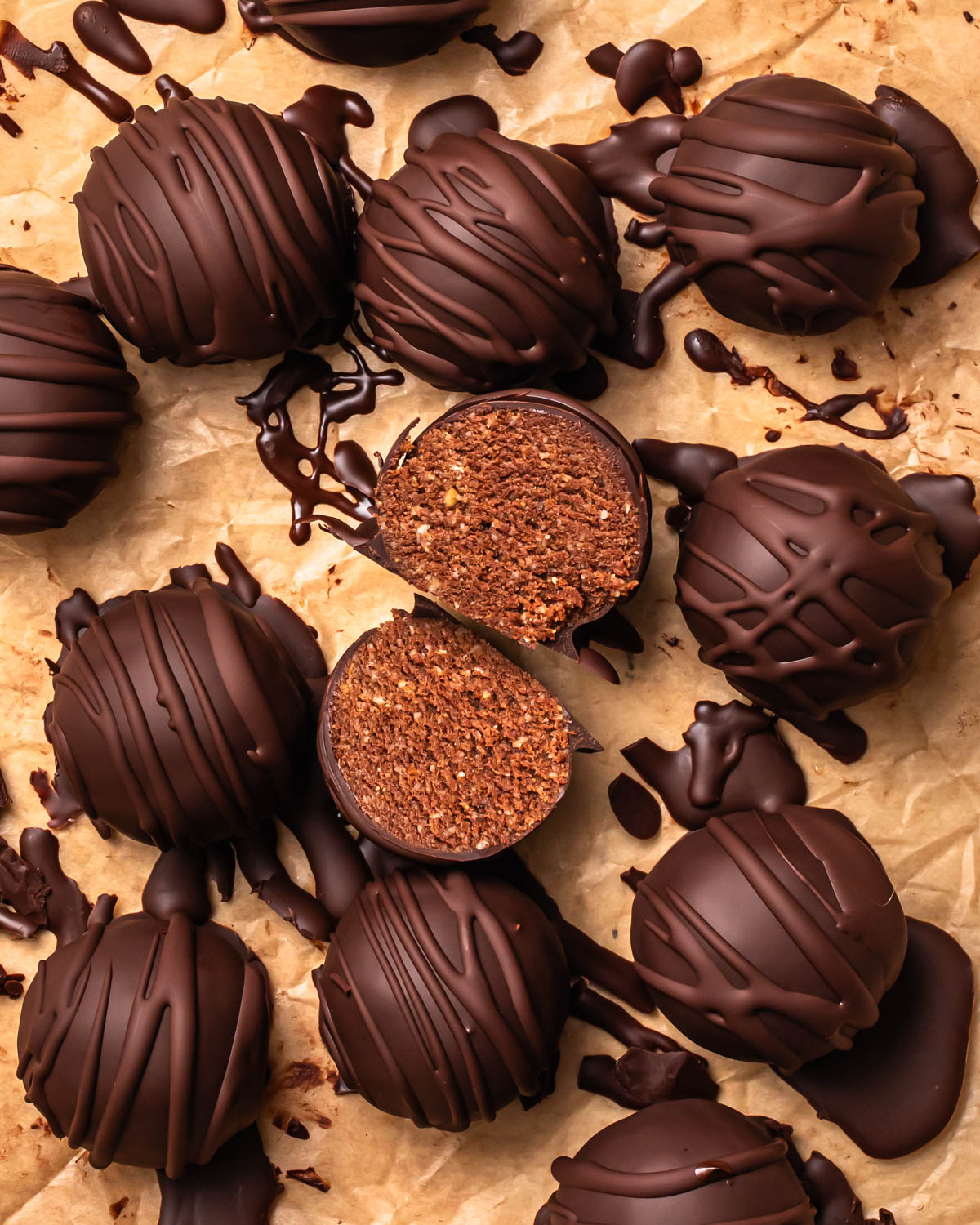 Double chocolate protein balls on a baking paper lined tray with one sliced in half to show the cake like centre. 