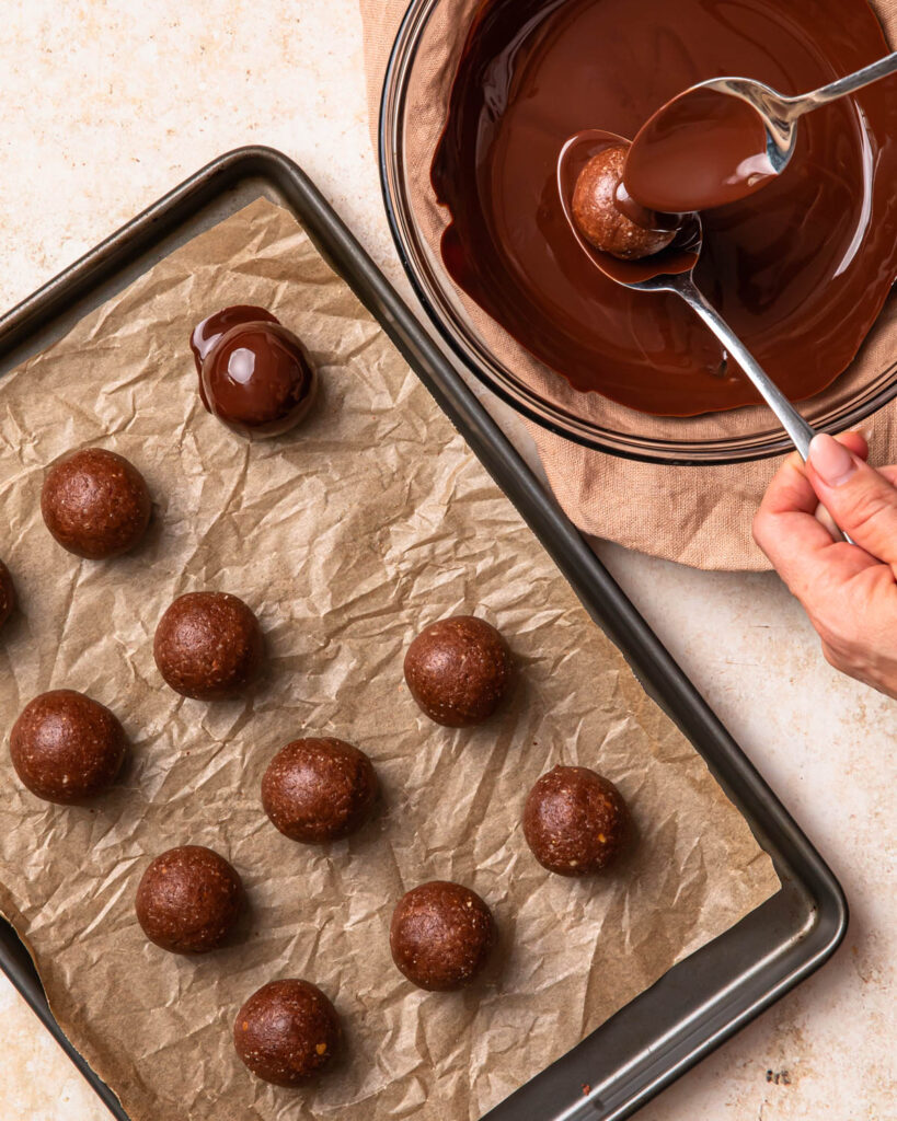 Chocolate protein balls being coated in melted dark chocolate.