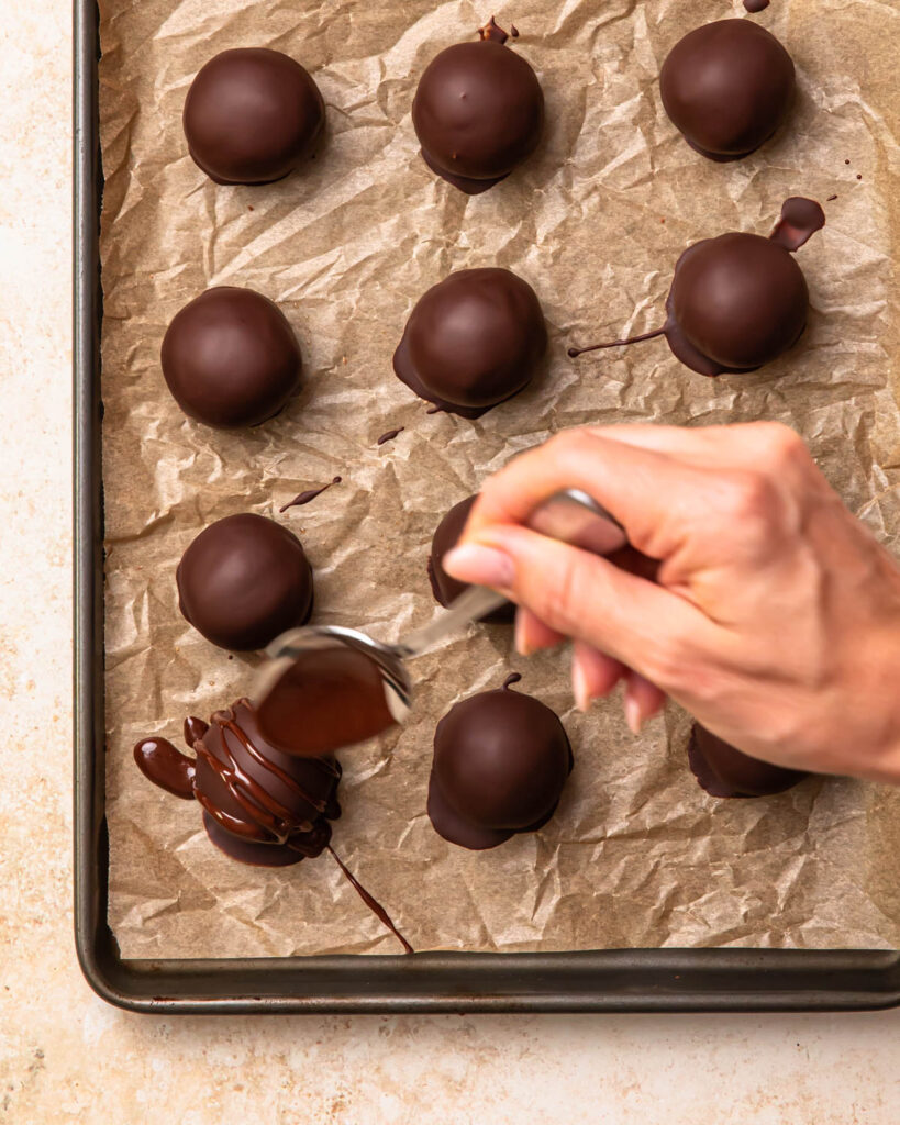 A hand drizzle melted dark chocolate over double chocolate protein balls.