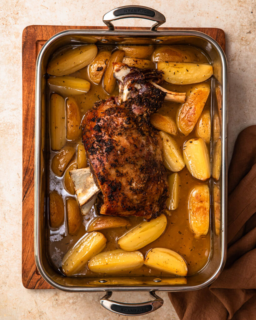 Crispy skinned slow cooked lamb shoulder and lemony potatoes in a roasting pan.