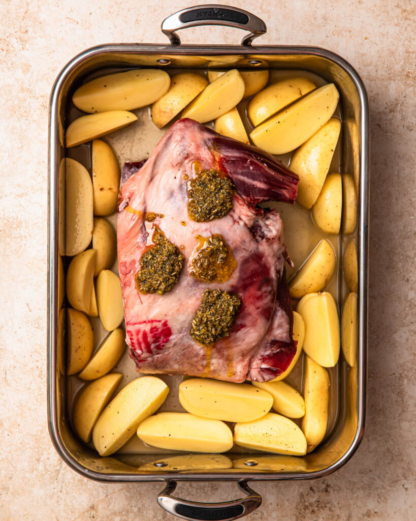 Lamb shoulder added to roasting pan with potato wedges, the lamb is topped with a lemon herb rub. 