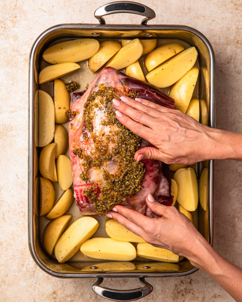 Two hands rubbing a lemon and herb rub into a lamb shoulder. 
