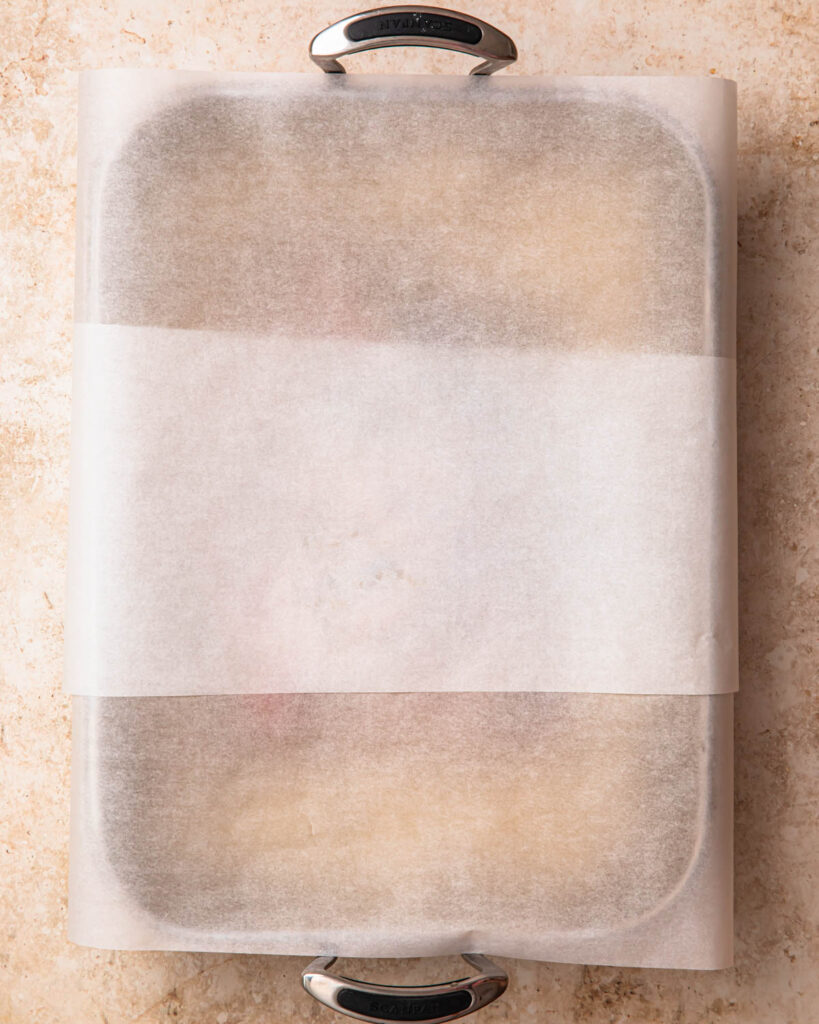 Roasting pan with lamb and potatoes covered with baking paper.