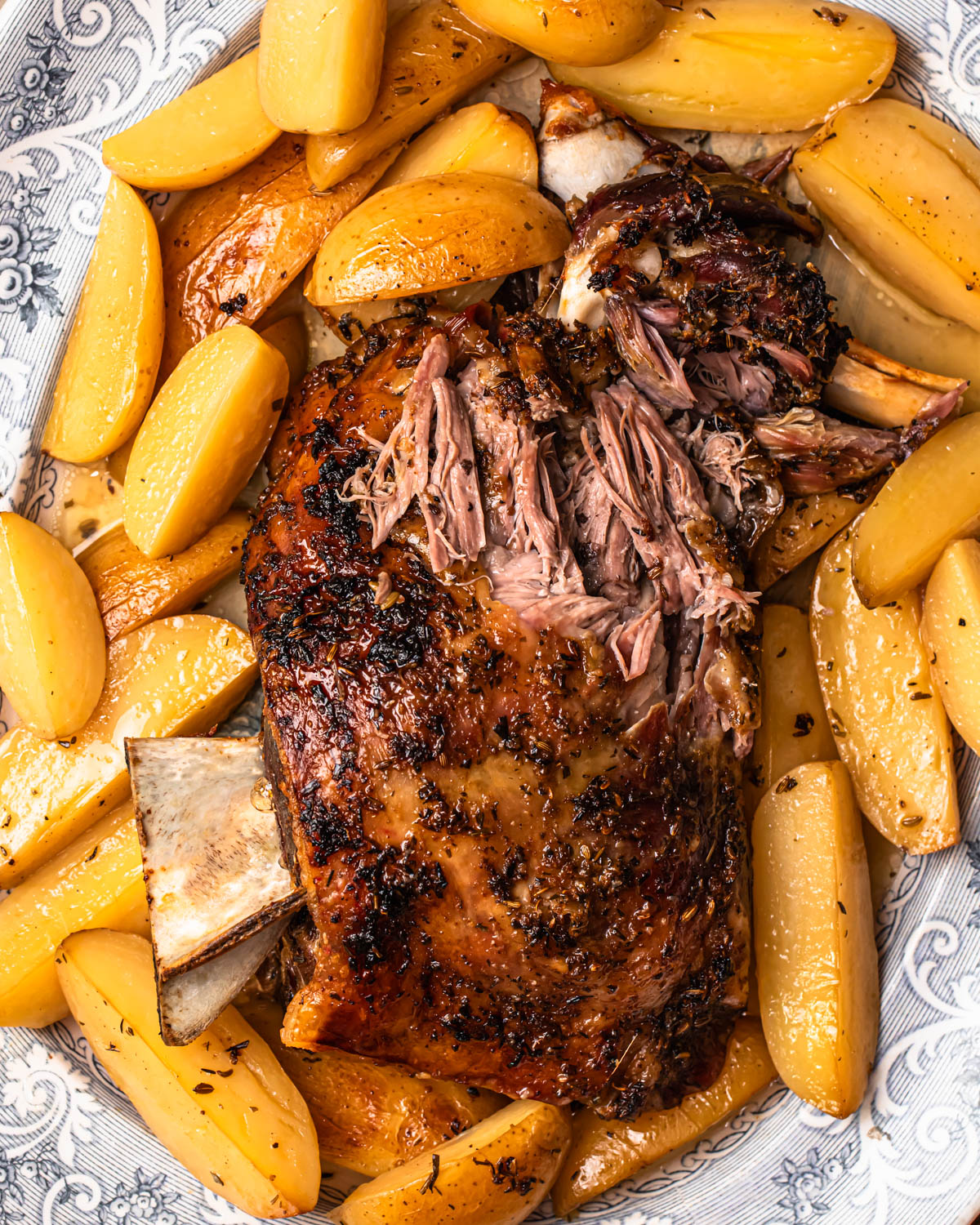 Close up photo of slow cooked lamb shoulder resting on a bed of lemony potatoes.