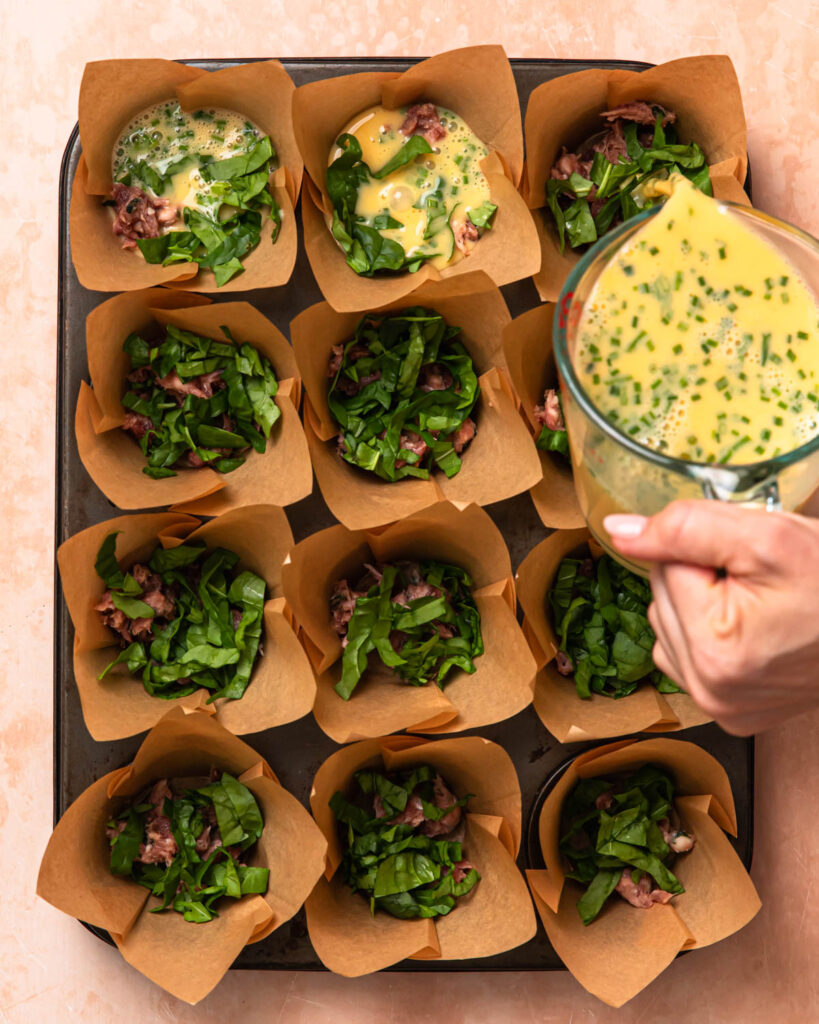 Egg mixture being poured into a muffin tin lined with muffin liners.