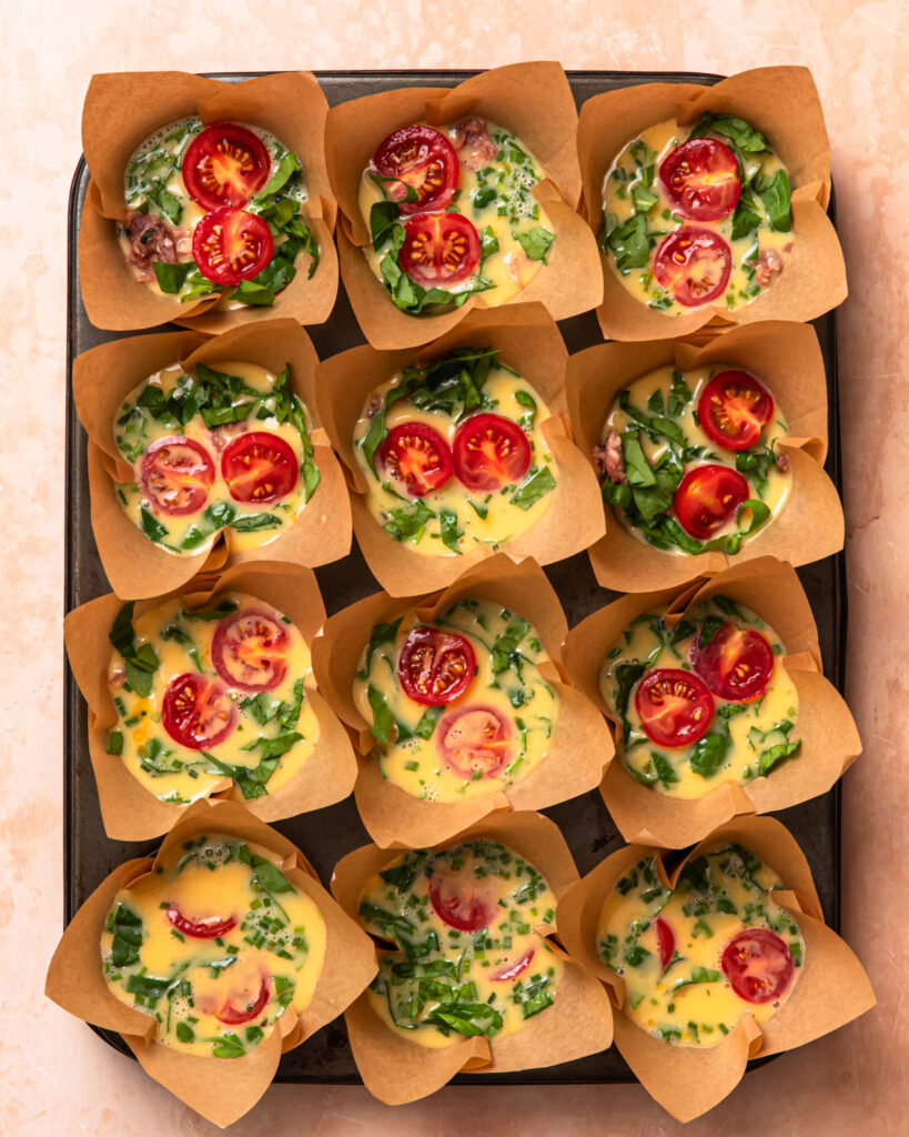Uncooked breakfast sausage egg cups topped with cherry tomato halves.
