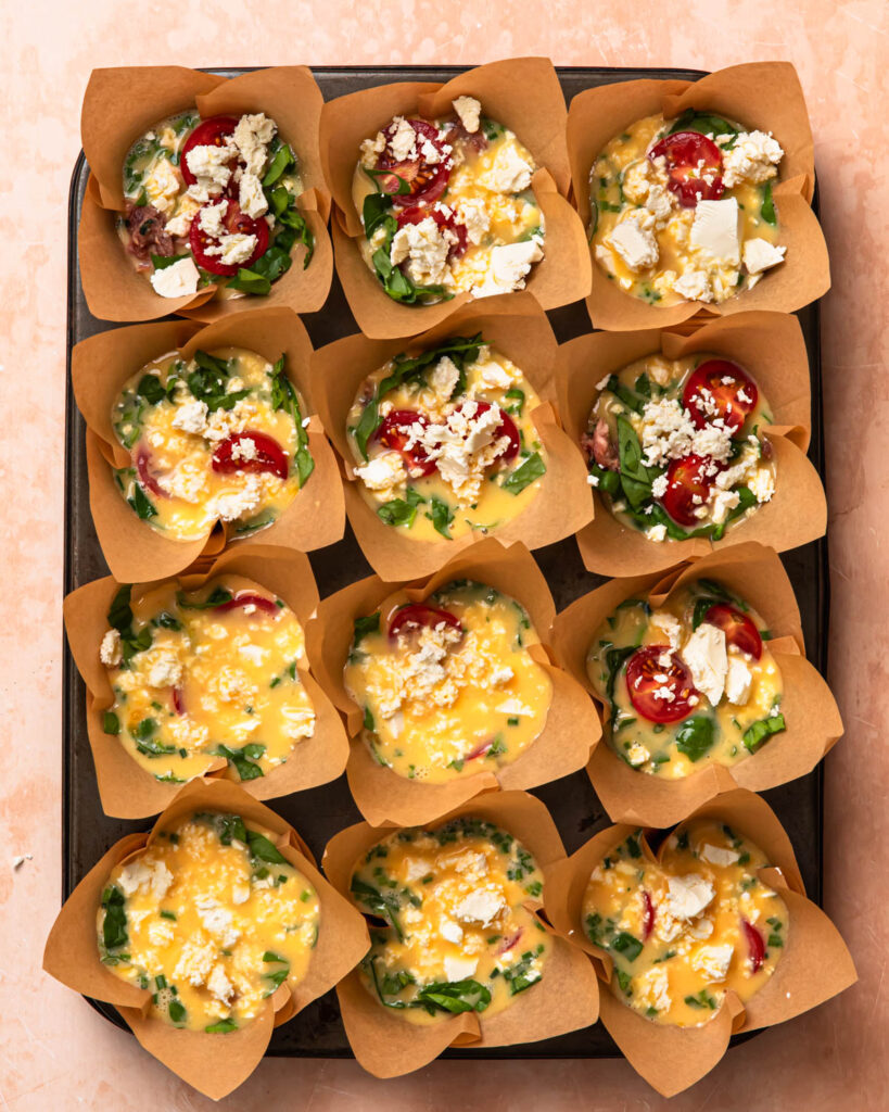Uncooked breakfast sausage egg cups topped with crumbled feta.