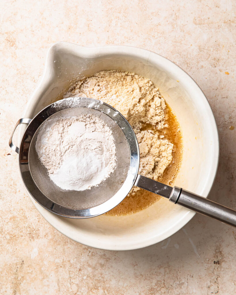 Dry ingredients being sieved into mixing bowl to make protein choc chip muffin batter.