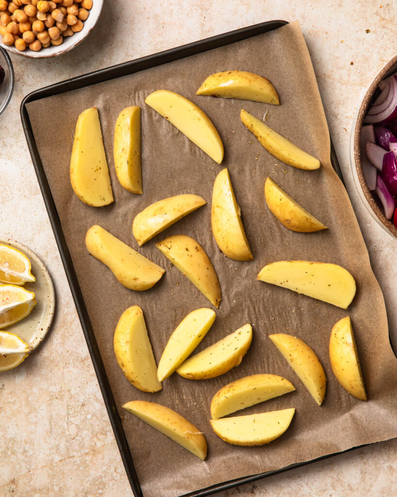 Seasoned potato wedges spread out on a baking paper lined tray.