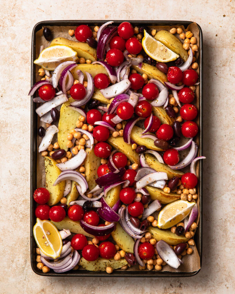 Cherry tomatoes, onions and lemon wedges added to a large sheet pan with roasted potatoes. 