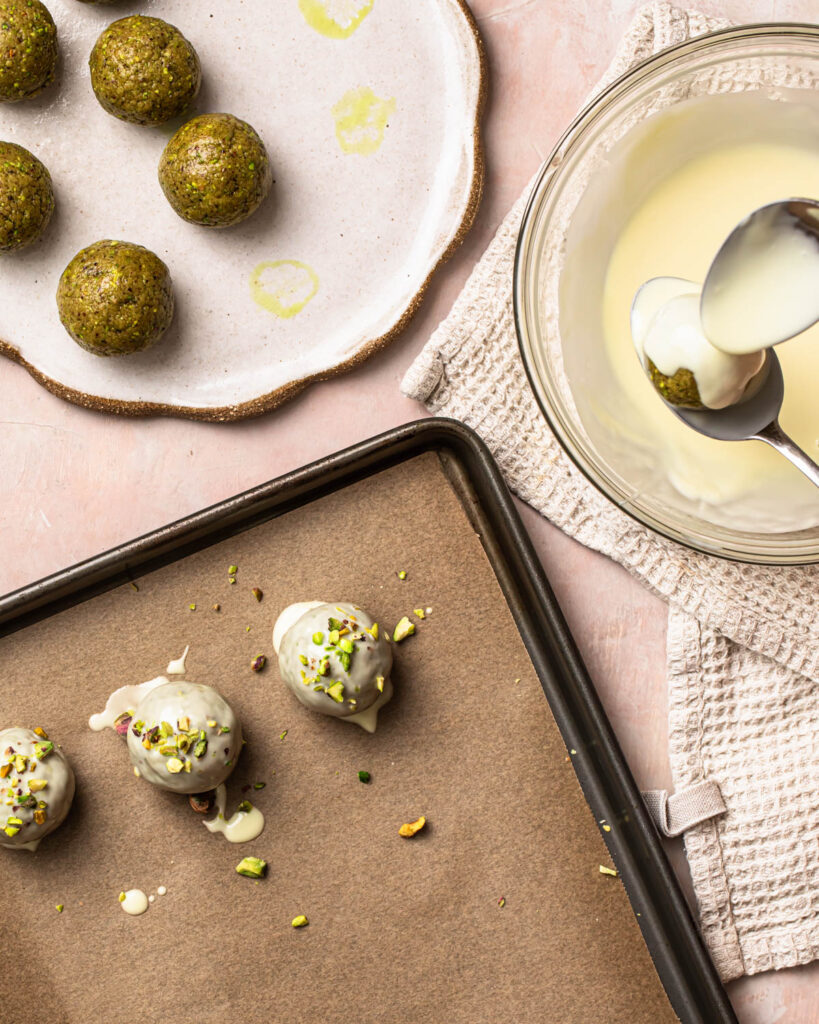 Pistachio protein balls being coated in melted white chocolate.
