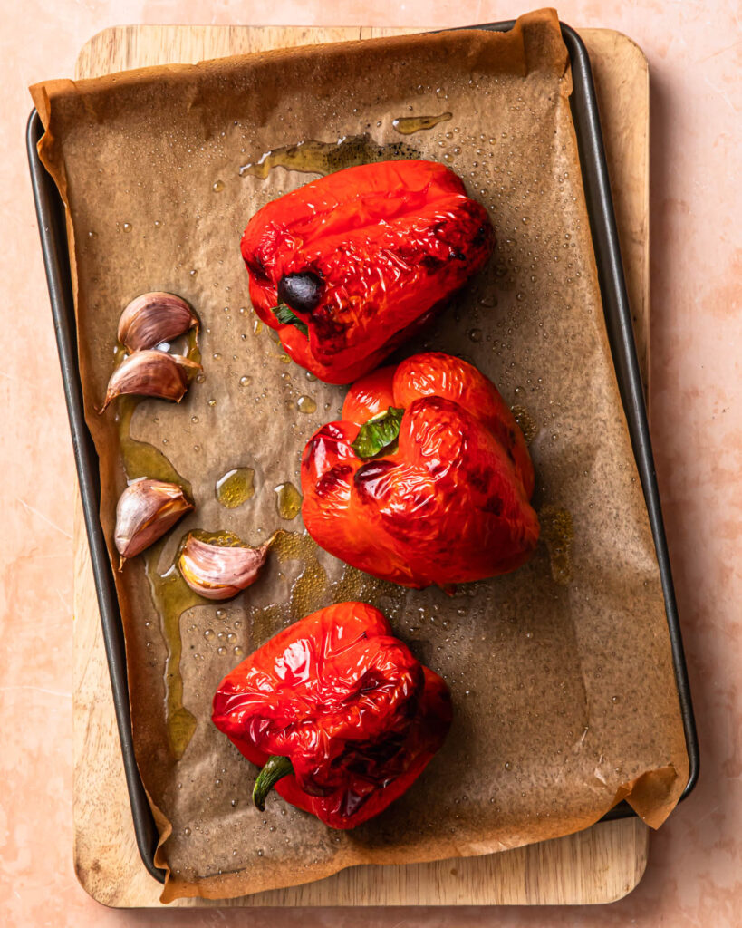 Roasted red peppers and garlic cloves on a baking tray.