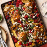 Mediterranean sheet pan chicken on a pan topped with crumbled feta and herbs.