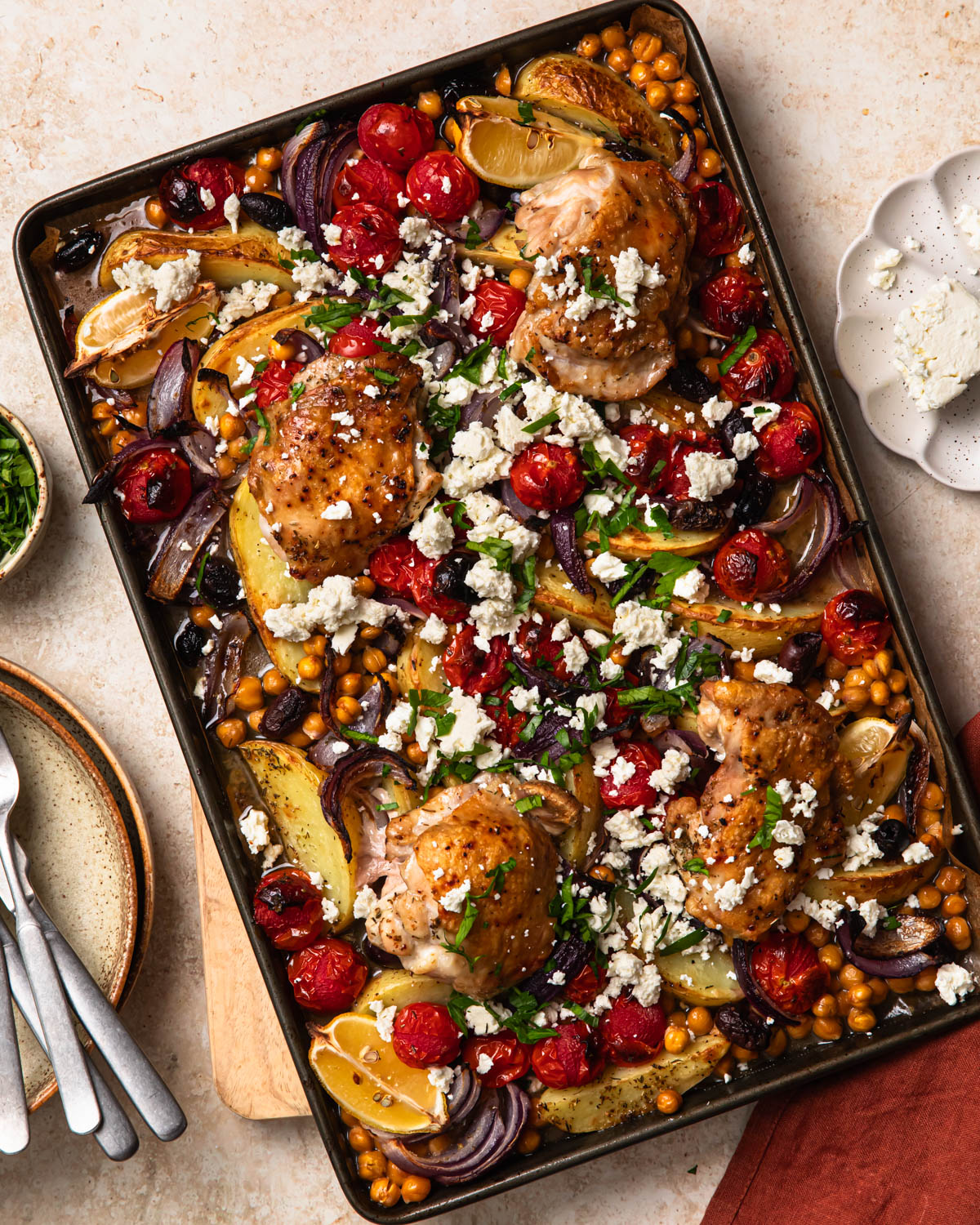 Mediterranean sheet pan chicken on a pan topped with crumbled feta and herbs.