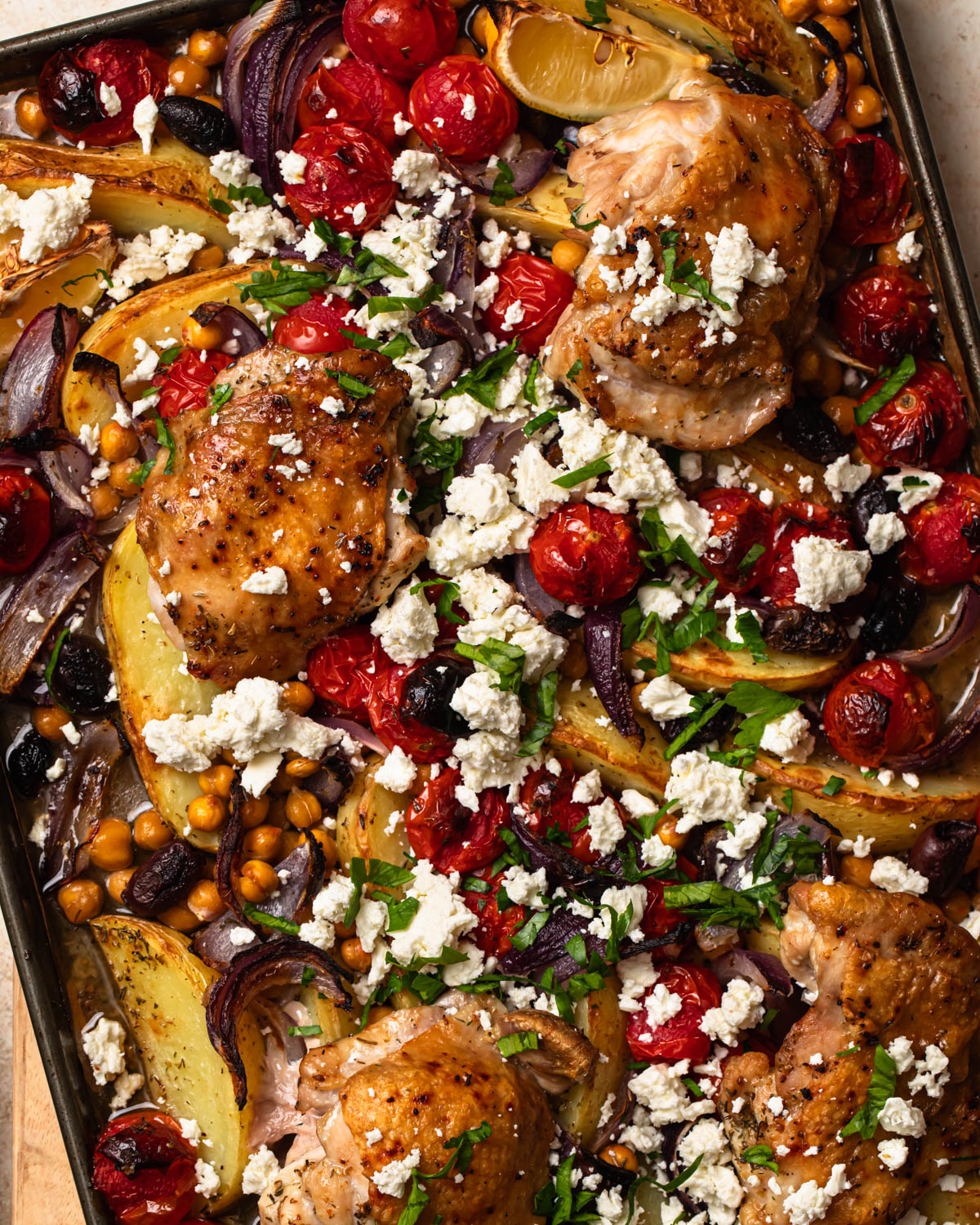 Close up of Mediterranean sheet pan chicken on a pan topped with crumbled feta and herbs.